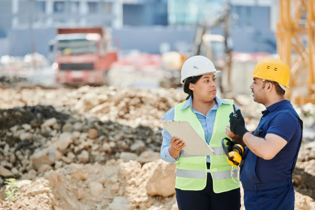 Construction professional with a clipboard discussing work with a contractor on a construction site