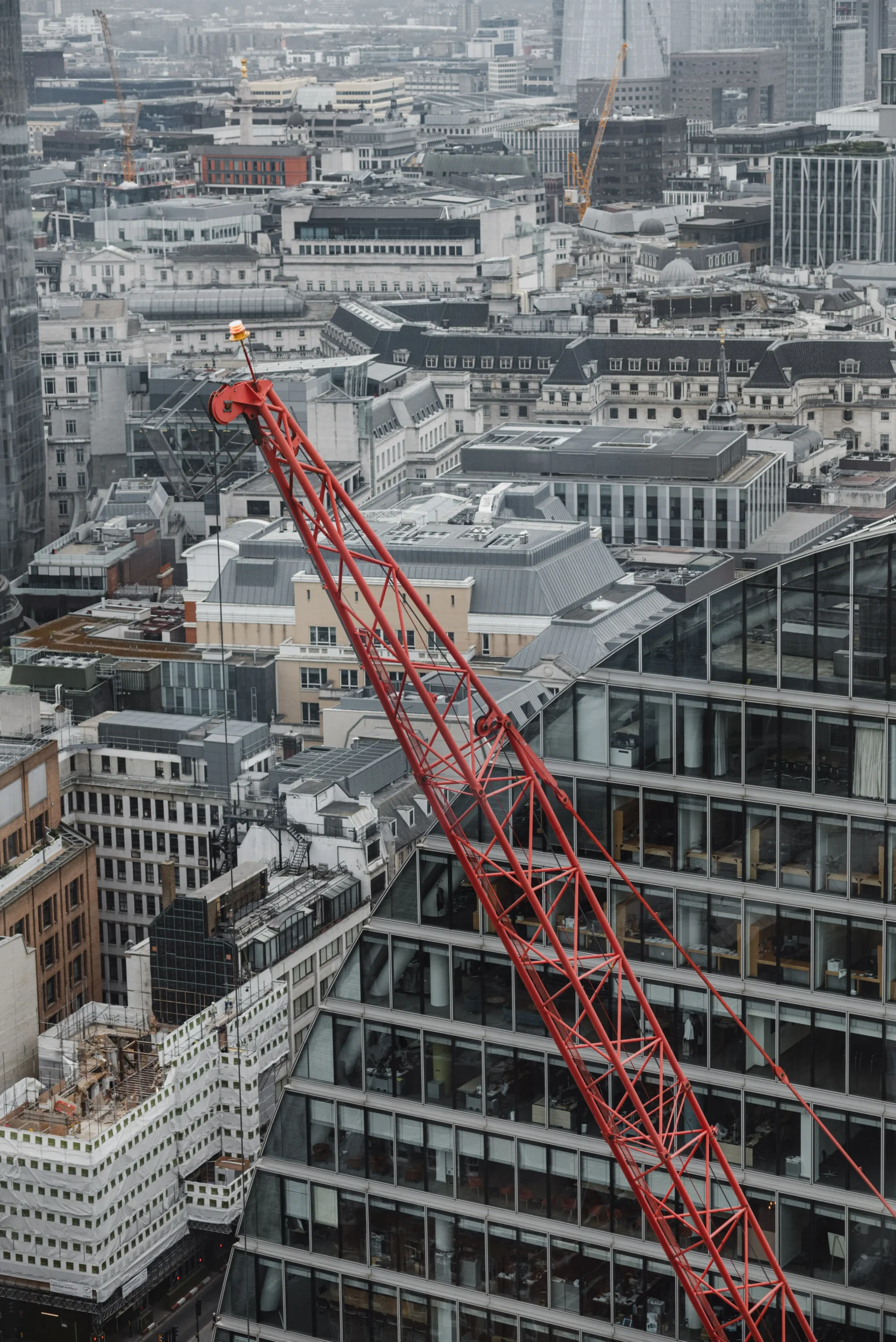 Red crane jib above office buildings in the City of London, with a scaffolded building under construction